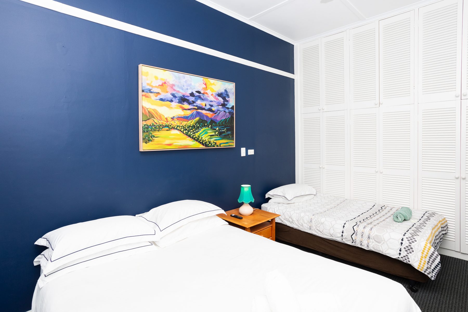 A guest room with a double bed, single bed and a colourful landscape painting